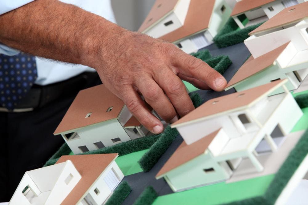 Image of a man's hand pointing at miniature models of ranch-style homes.